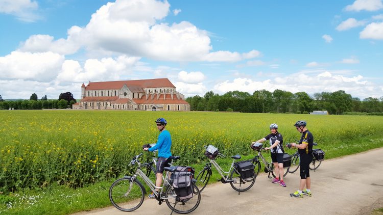 trois cyclistes devant une champ avec une vue sur l'abbaye de pontigny