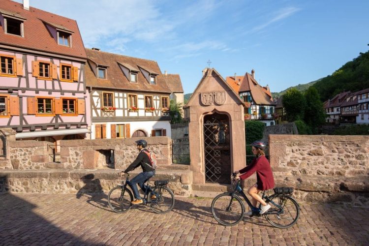 Fahrradfahrer auf einer Brücke umgeben von Fachwerkhäusern im Elsass